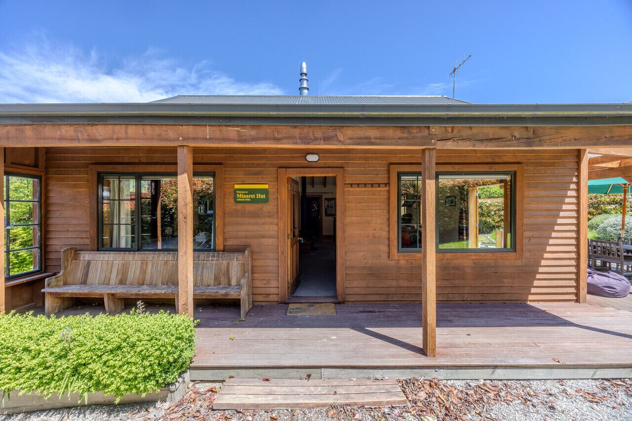 A wooden lodge with a porch, benches, and a sign indicating it's the Minaret Hut.