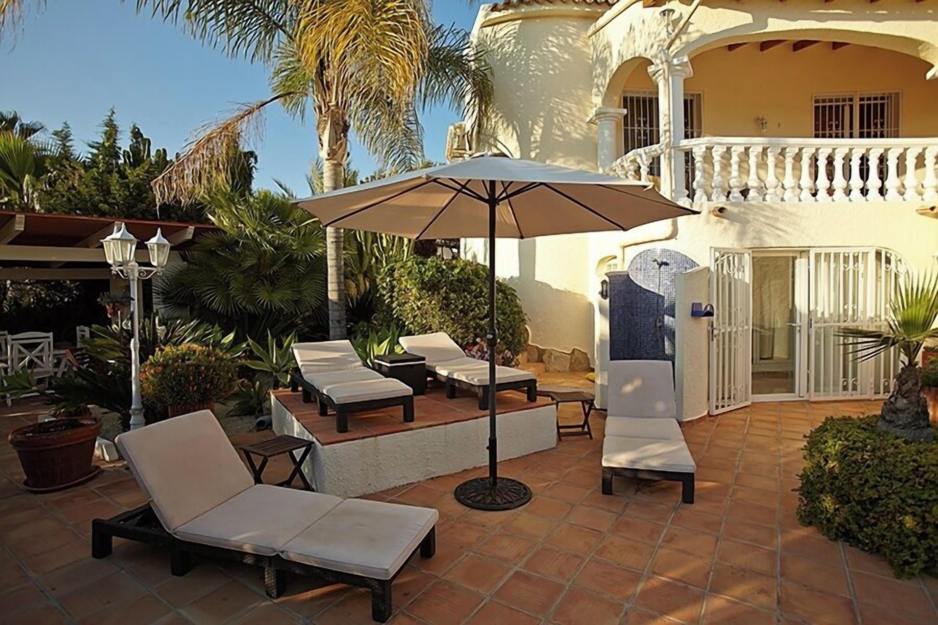 Un patio al aire libre con sillones de descanso, una sombrilla grande y plantas en macetas.