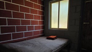 A small, single-bed room with a brick wall and a window. - Kodachadri Pathalagere Homestay (Hosanagara)