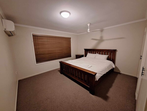 A bedroom with a single bed, a ceiling fan, a window with blinds, and an air conditioning unit.