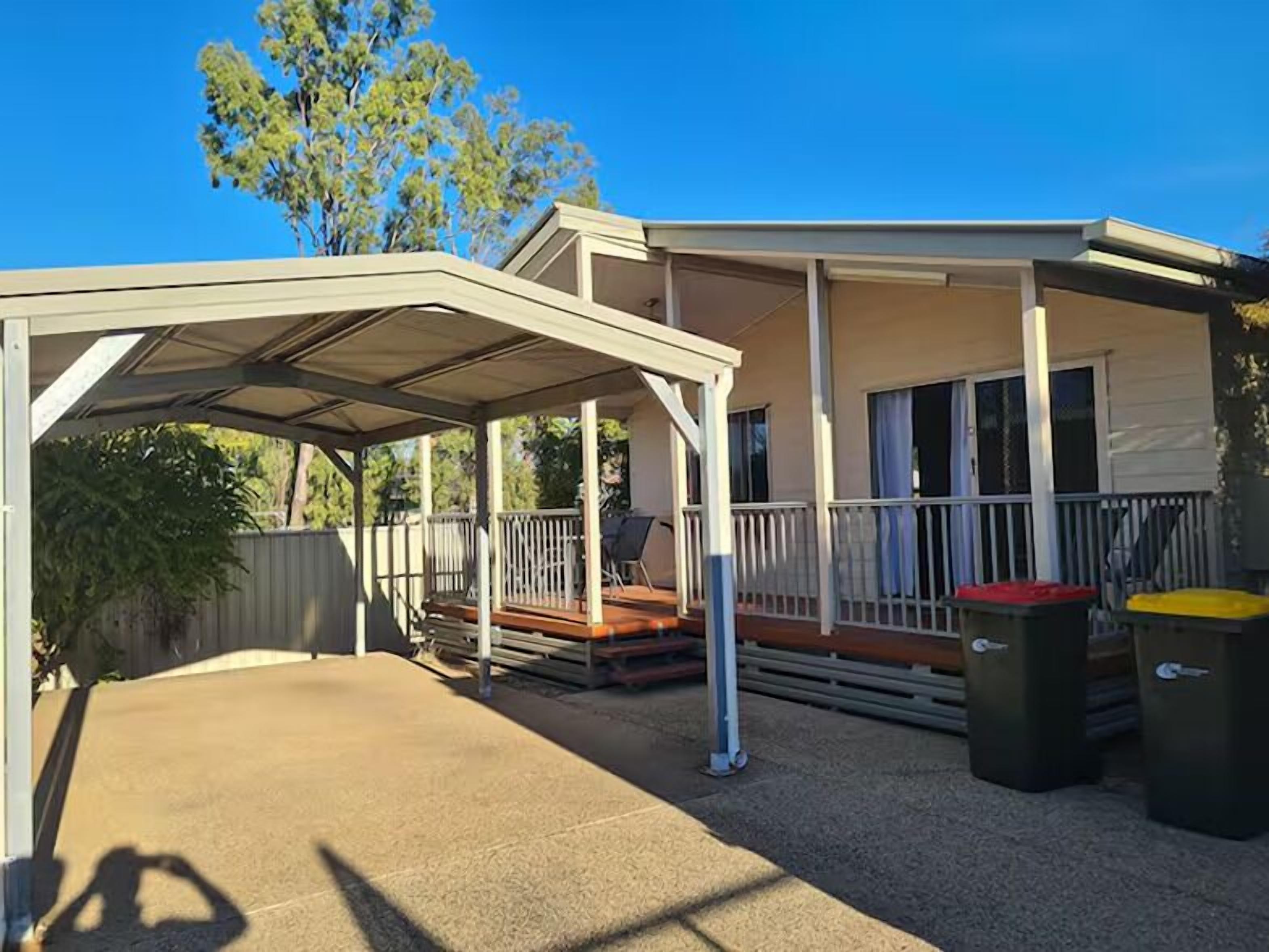 A covered outdoor area with a patio, a covered deck, and a building with windows and a balcony.