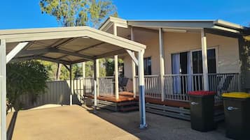 A covered outdoor area with a patio, a covered deck, and a building with windows and a balcony.
