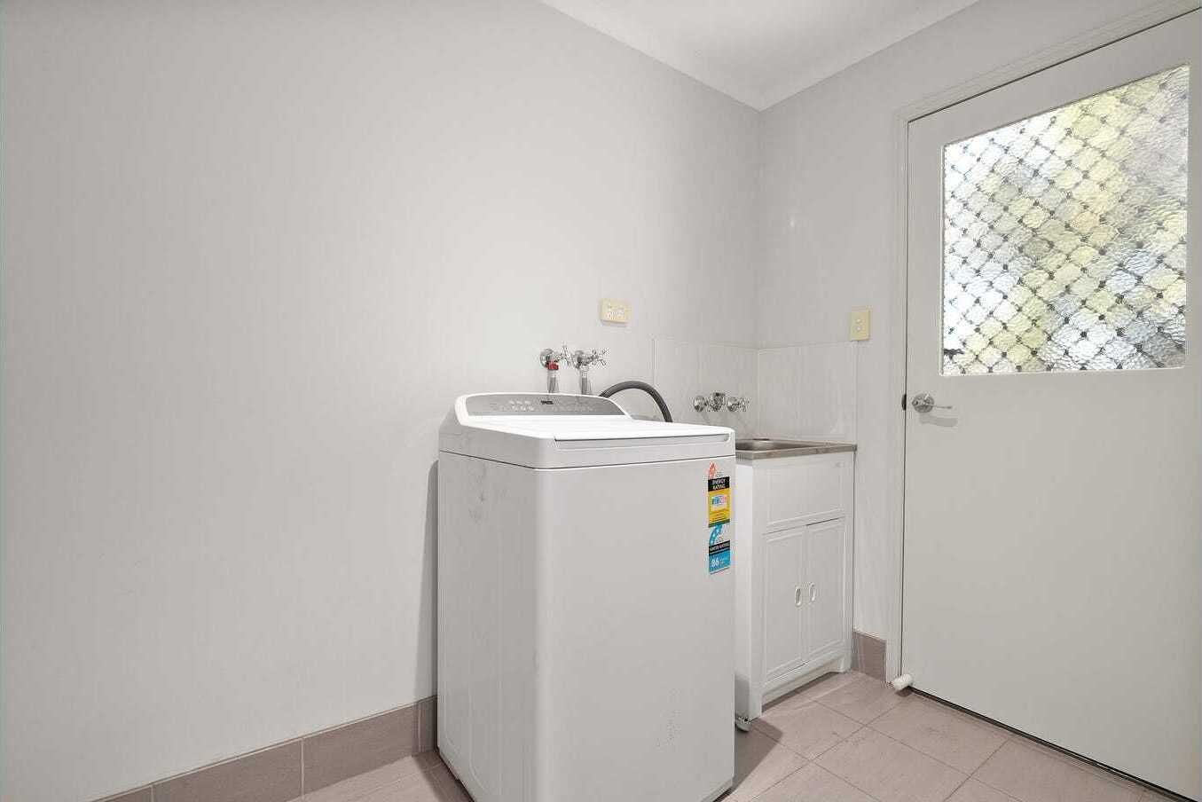 A compact laundry room with a washing machine, a sink, and a door with a window.
