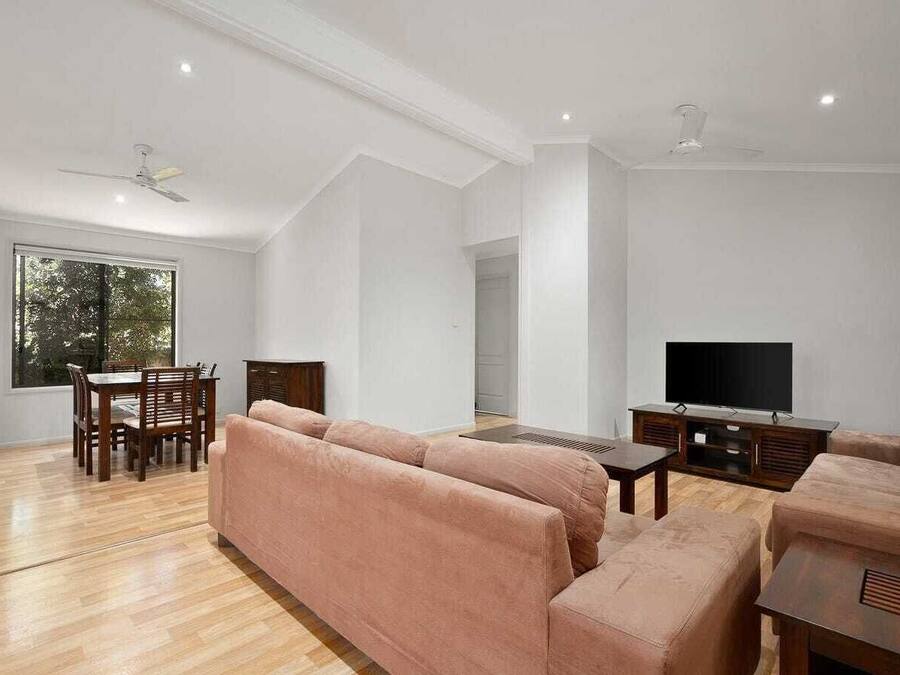 Amplia sala de estar con un ventanal, comedor con mesa y sillas, y televisor sobre un mueble de madera.