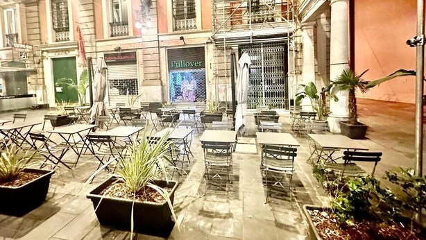 Un área de estar al aire libre con mesas y sillas, rodeada de plantas en macetas.