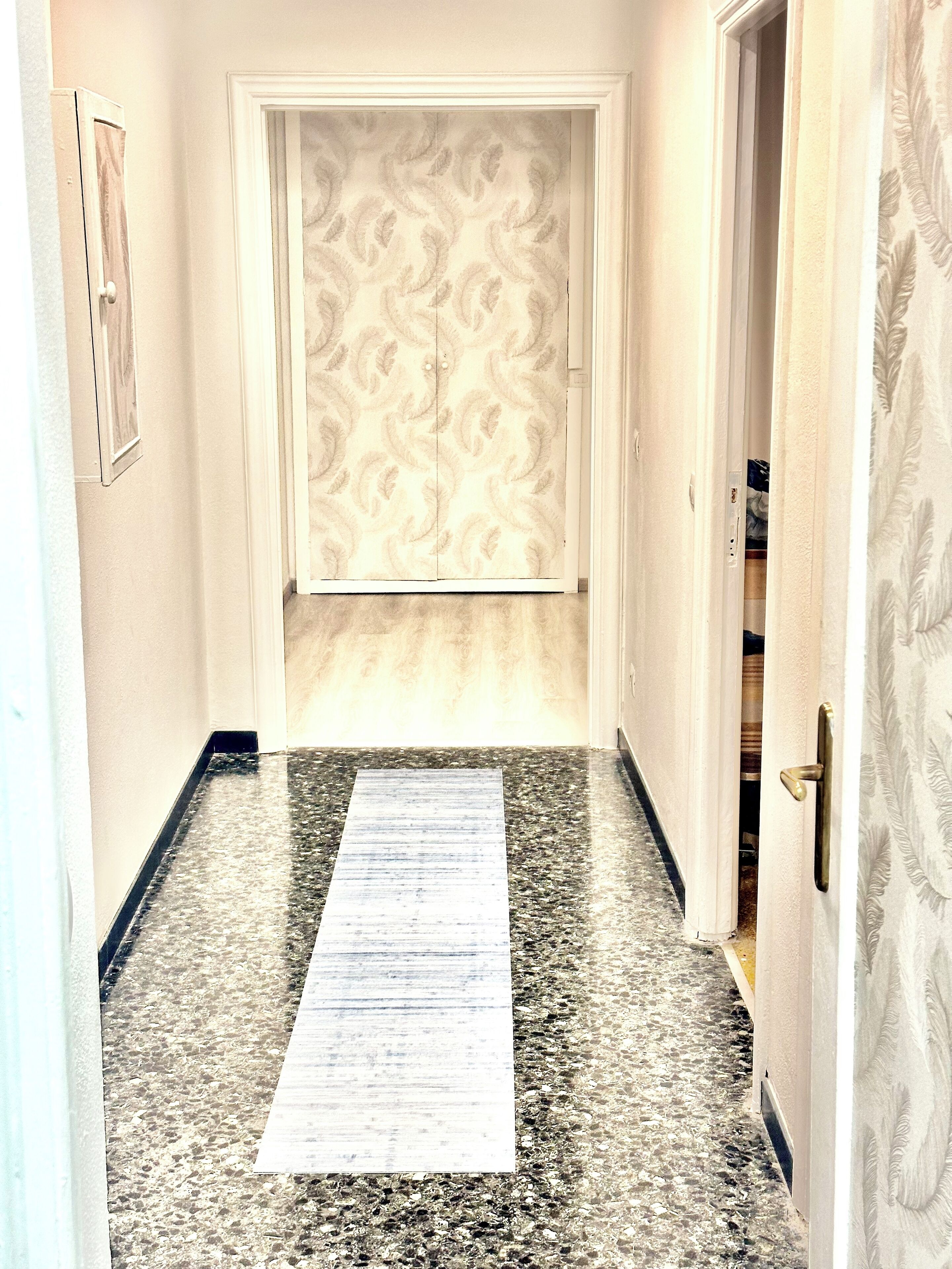 Un couloir avec un papier peint à motifs, un sol en marbre et une porte dotée d’une poignée en laiton.