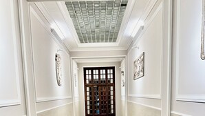 Un pasillo con piso de mármol, paredes blancas y una puerta grande de madera con paneles de vidrio.