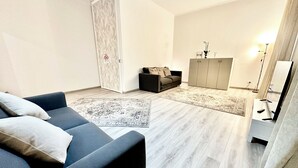 Una sala de estar moderna con un sofá gris, un sillón oscuro, un tapete estampado, un armario gris y una lámpara de pie.