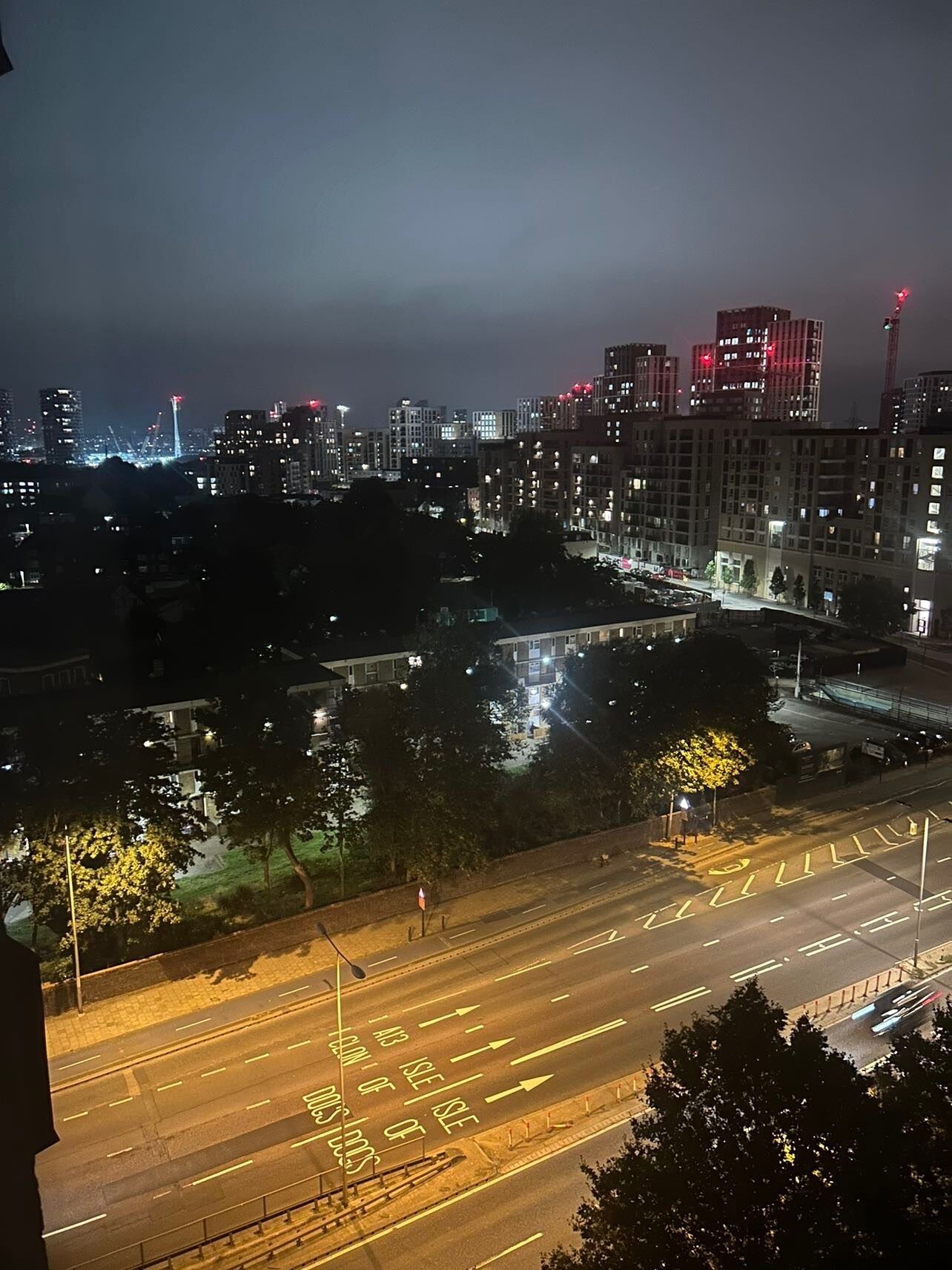 A nighttime cityscape with illuminated buildings and a multi-lane road with directional arrows.