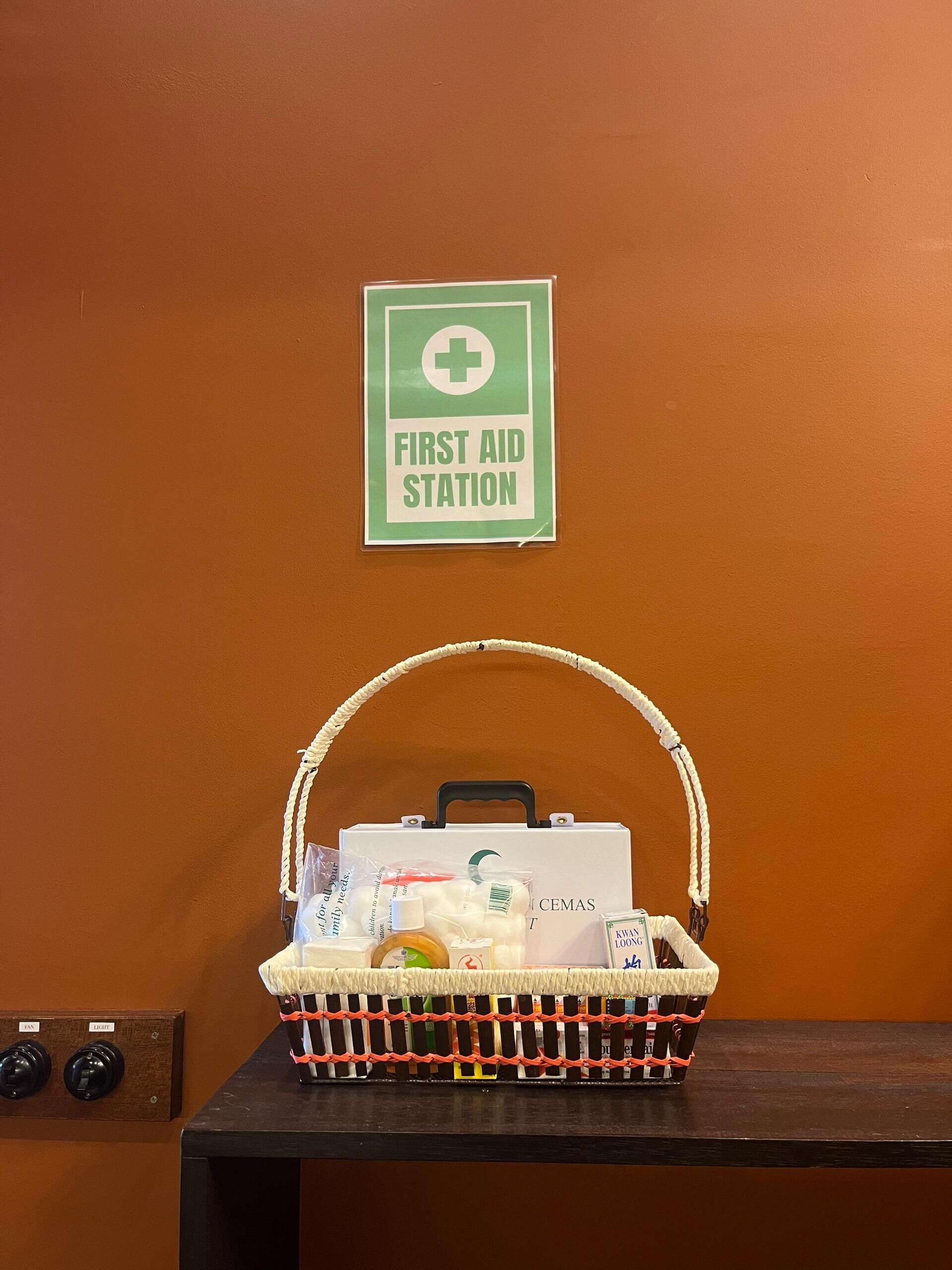 A first aid station sign on an orange wall, a basket with various items on a table below.