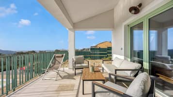 A balcony with a view of a building and mountains, furnished with a sofa, chairs, and a table.