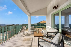 Un balcon donnant sur un immeuble et des montagnes, aménagé avec un canapé, des chaises et une table.