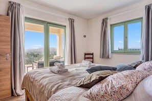 Un dormitorio con cama, almohadas, ventana y vistas al exterior.