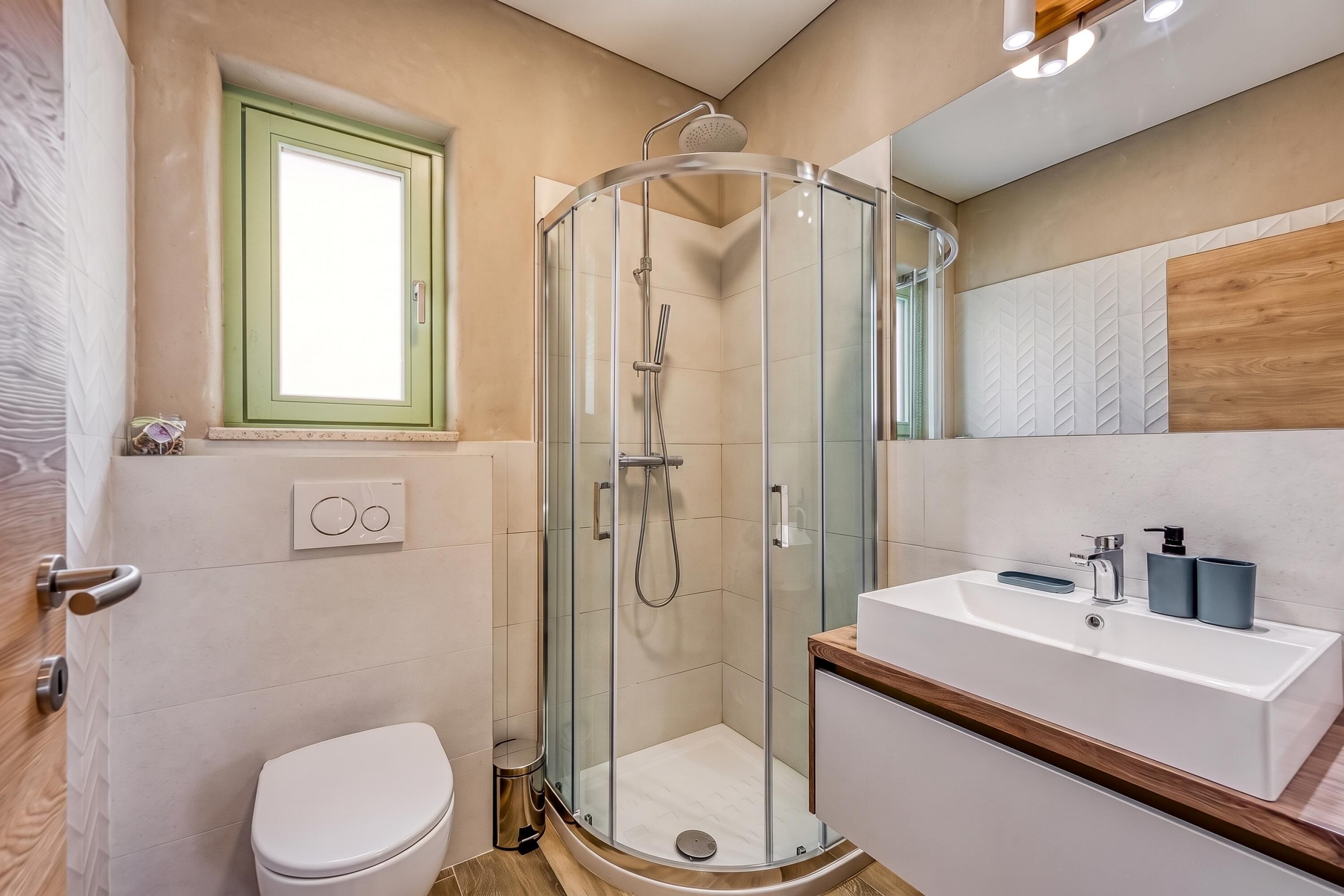 Un baño moderno con cabina de ducha de vidrio, inodoro y lavabo con encimera de madera.