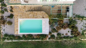 An aerial view of a property with a swimming pool, stone patio, and surrounding greenery.