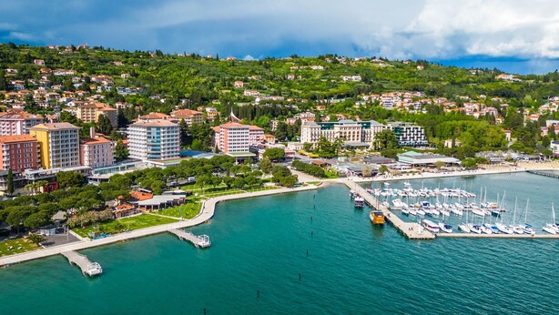 A coastal town with a marina, buildings, and a hilly backdrop.