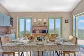 Een eetgedeelte met een tafel voor vier personen, keukenkastjes, een raam en uitzicht op een balkon.