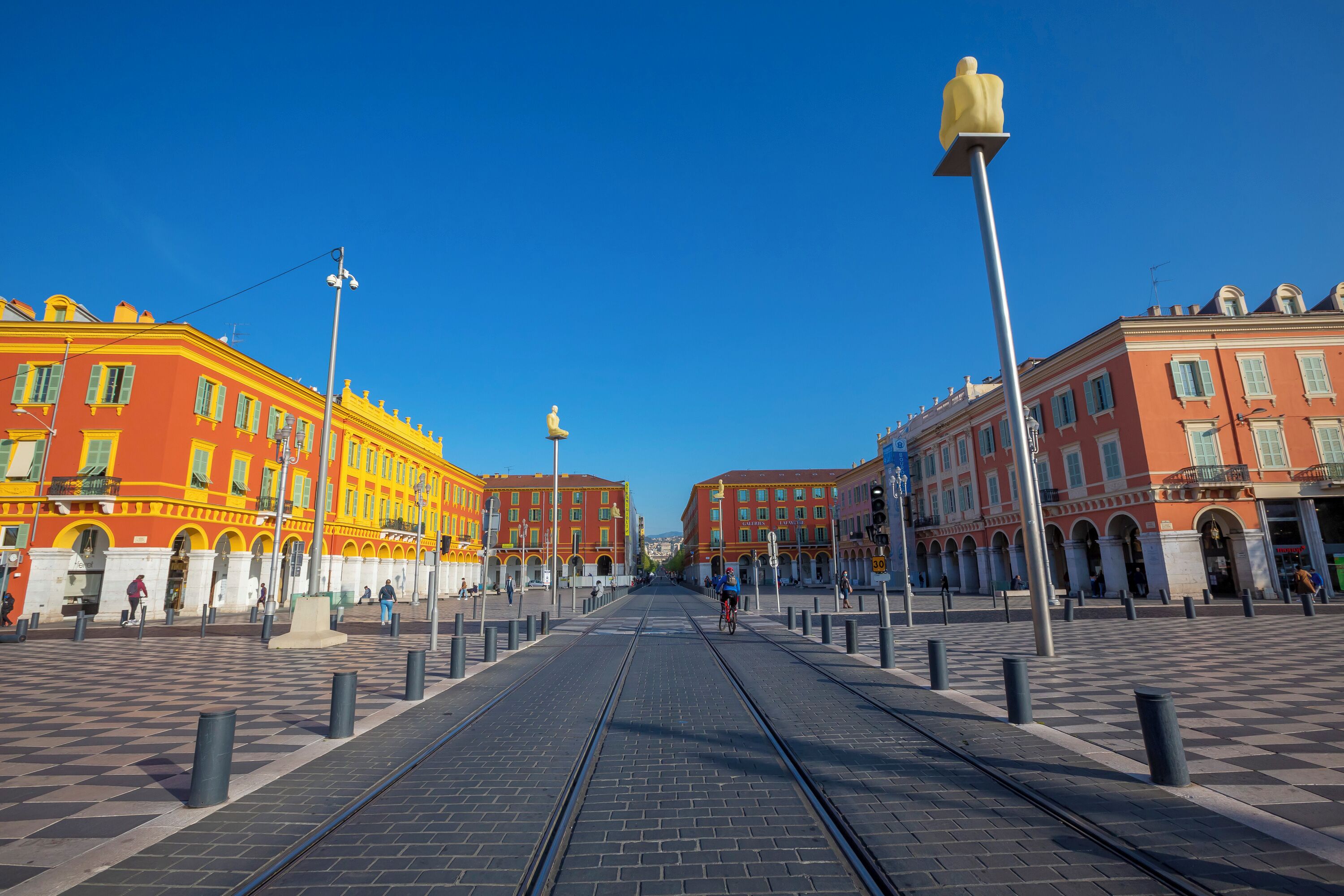 A tram track leading to a plaza with colorful buildings and a clear blue sky.