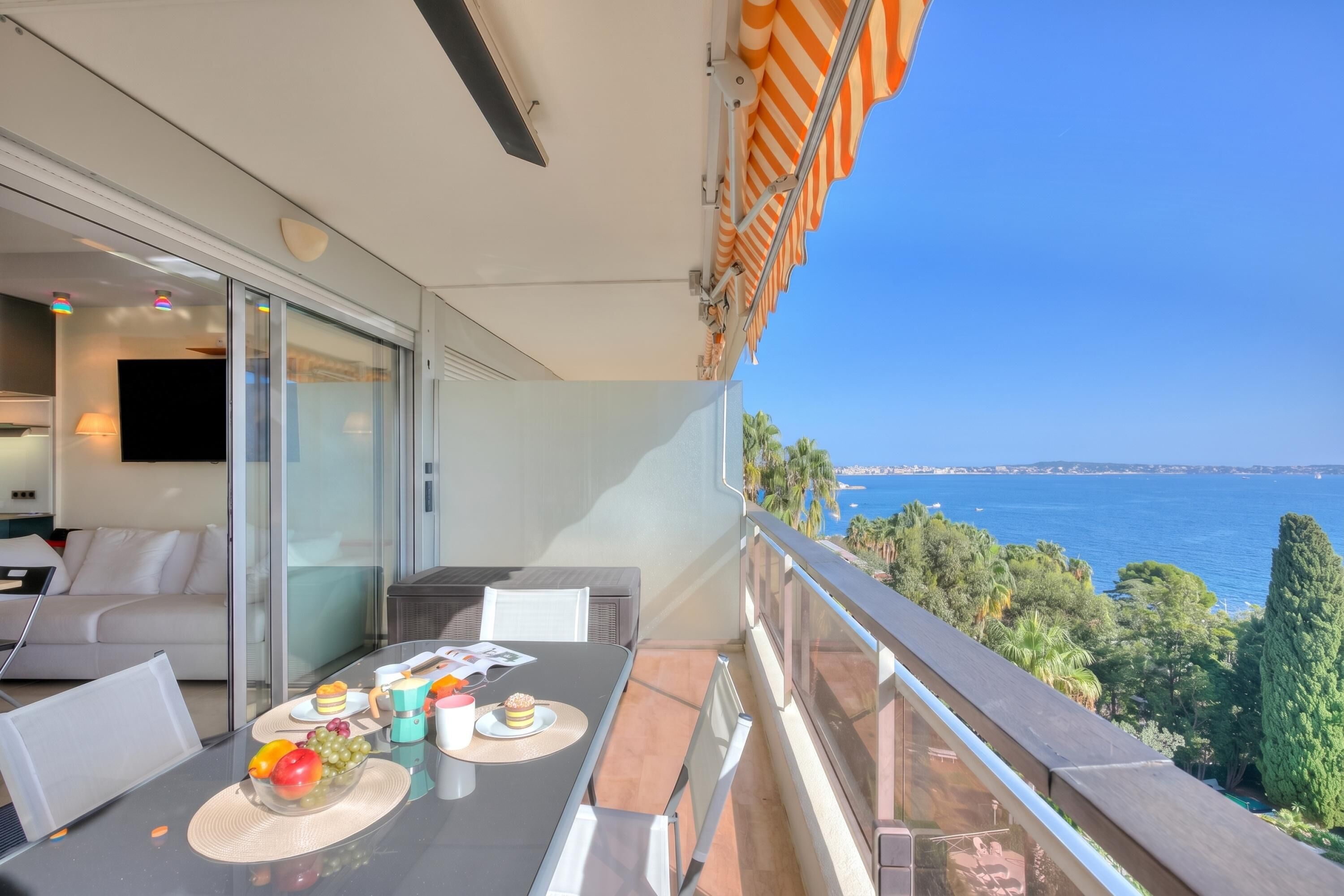 A balcony with a table set for dining, a sofa, and a view of the sea.