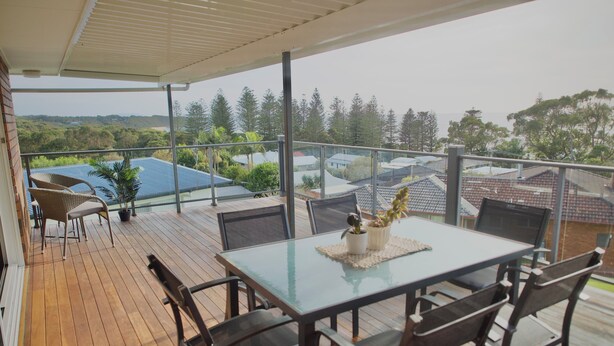 A covered outdoor area with a table and chairs, potted plants, and a view of surrounding buildings and greenery.