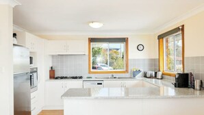 A modern kitchen with white cabinets, a central island, a window with a view, and a clock on the wall.