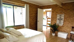 A bedroom with a large bed, a potted plant, a hanging wall decoration, and a view of the outside.