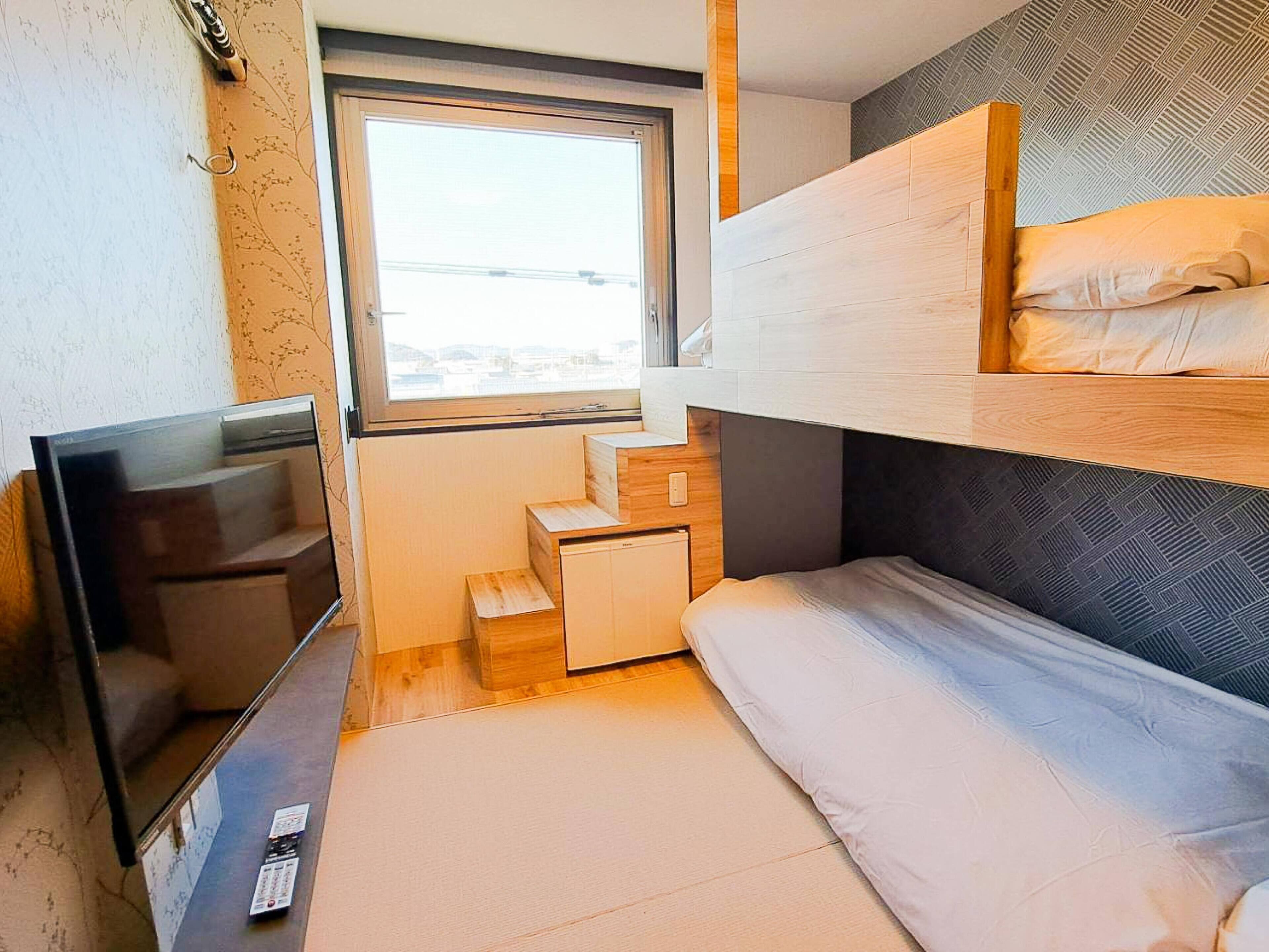 Habitación pequeña con literas, televisor, un mueble de madera y ventana con vistas al exterior.
