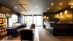 A modern hotel lobby with a seating area, a refrigerator stocked with snacks, and a reception desk. - Hotel Areaone Naruto (Naruto)