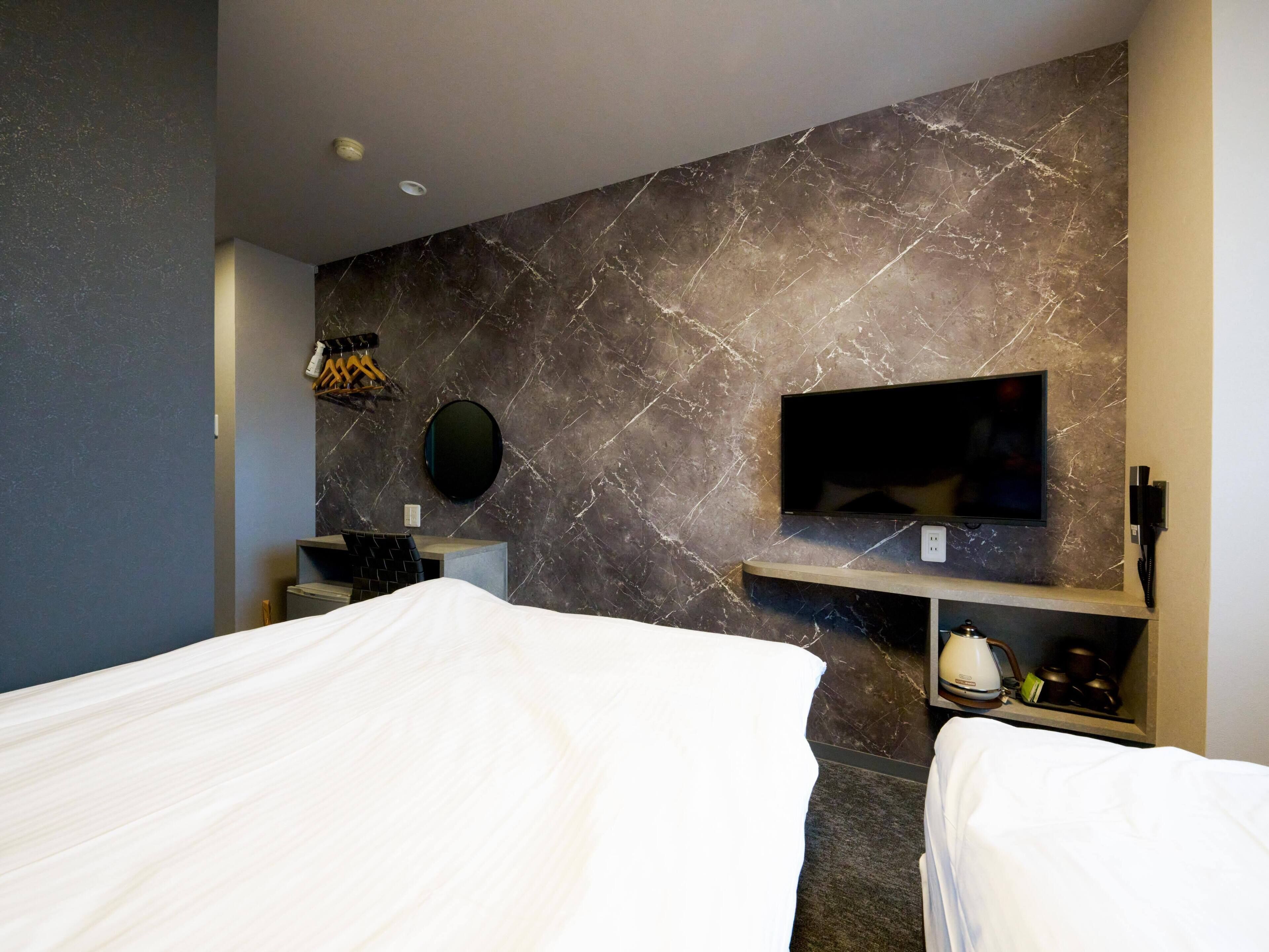 A modern hotel room with a marble wall, a flat-screen TV, a desk, and a bed with white bedding.