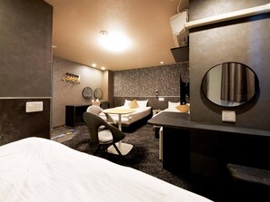 Une chambre d’hôtel moderne avec un grand lit, un bureau et une chaise. On y trouve deux tables de chevet, un miroir et un téléviseur fixé au mur.