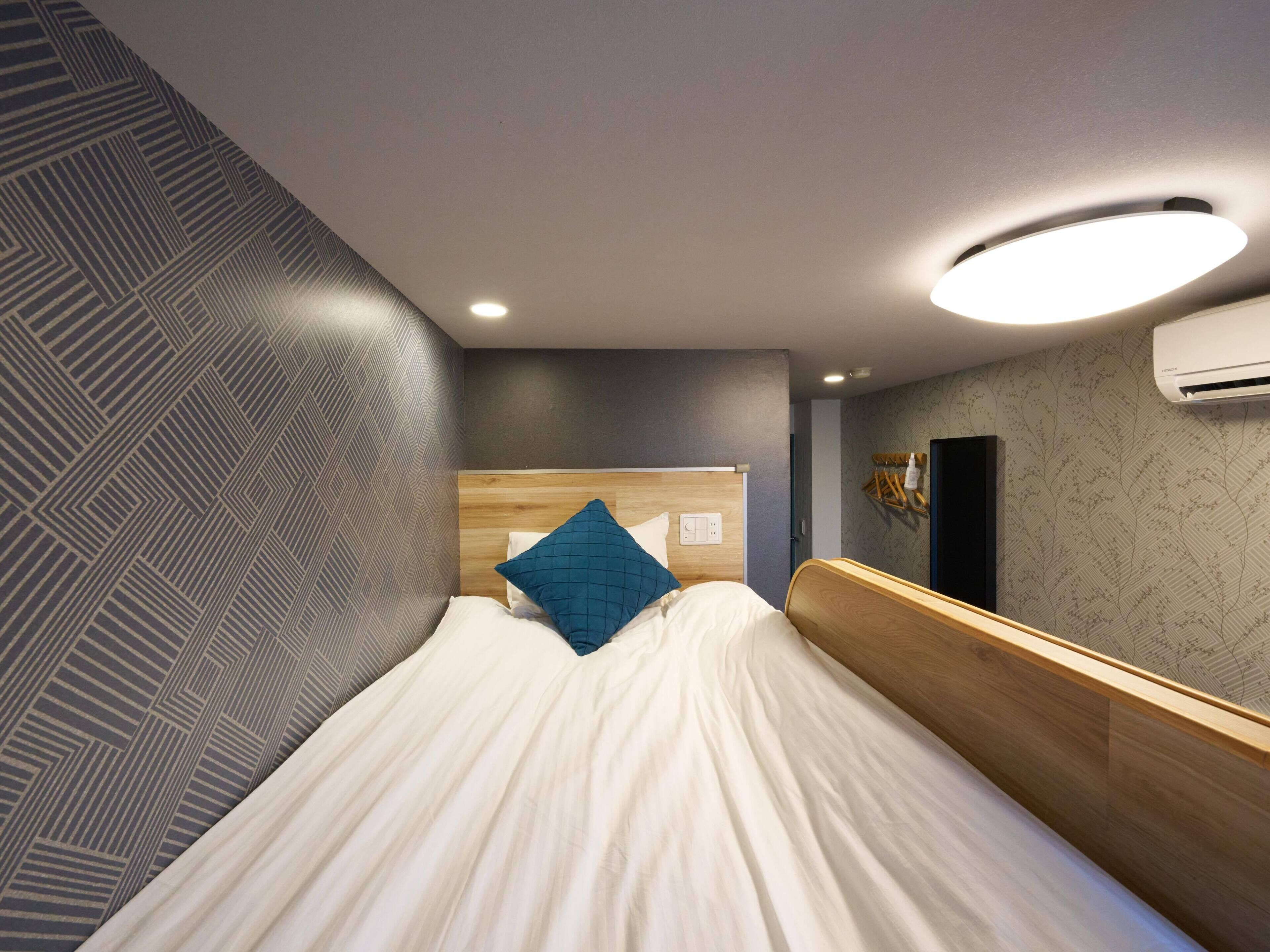 A modern hotel room with a bed, a headboard, a wall-mounted air conditioner, and a patterned wall.