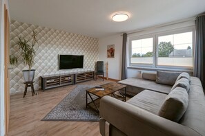 A modern living room with a large flat-screen TV, a sofa, a coffee table, and a potted plant.