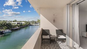 A balcony with two wicker chairs and a small table, overlooking a marina with boats and palm trees. - Bay Harbor Sunset Apt 5C (Bay Harbor Islands)