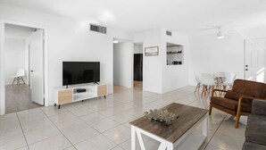 A modern living room with a flat-screen TV, a coffee table, and a sofa. There is a dining area with a table and chairs. - Bay Harbor Sunset Apt 5C (Bay Harbor Islands)