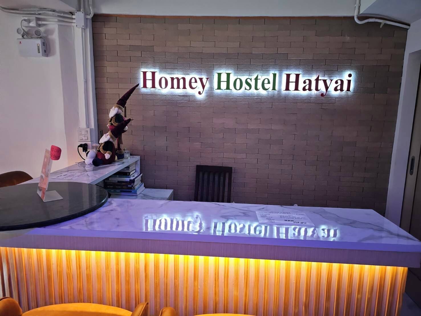 A reception desk with a sign reading 'Homey Hostel Hatyai' and a plush toy on the counter.