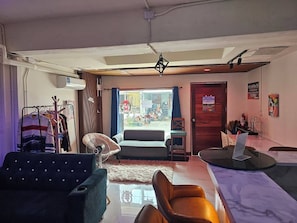 A room with a sofa, a chair, a table, a fan, and a view of the street outside.