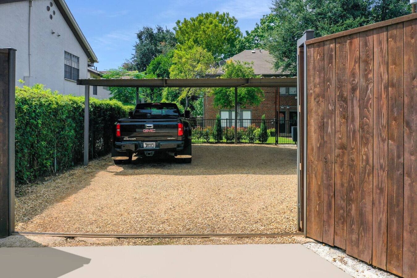 A gravel driveway leading to a garage with a wooden fence and a covered carport.