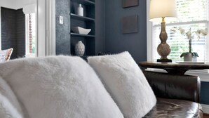 Una habitació amb una paret blau fosc, un sofà blanc amb coixins mullats, una taula auxiliar de fusta amb una làmpada i una estant amb objectes decoratius.