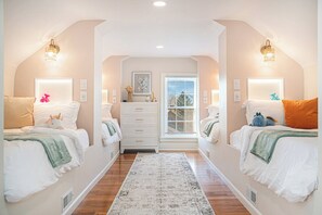 Een slaapkamer met twee bedden, een dressoir en een raam met jaloezieën.