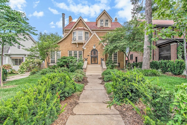 A two-story house with a front entrance, a pathway leading to the door, and a well-maintained garden with various shrubs and trees. - Dundee Gem, heated salt water pool, holiday décor (Omaha)