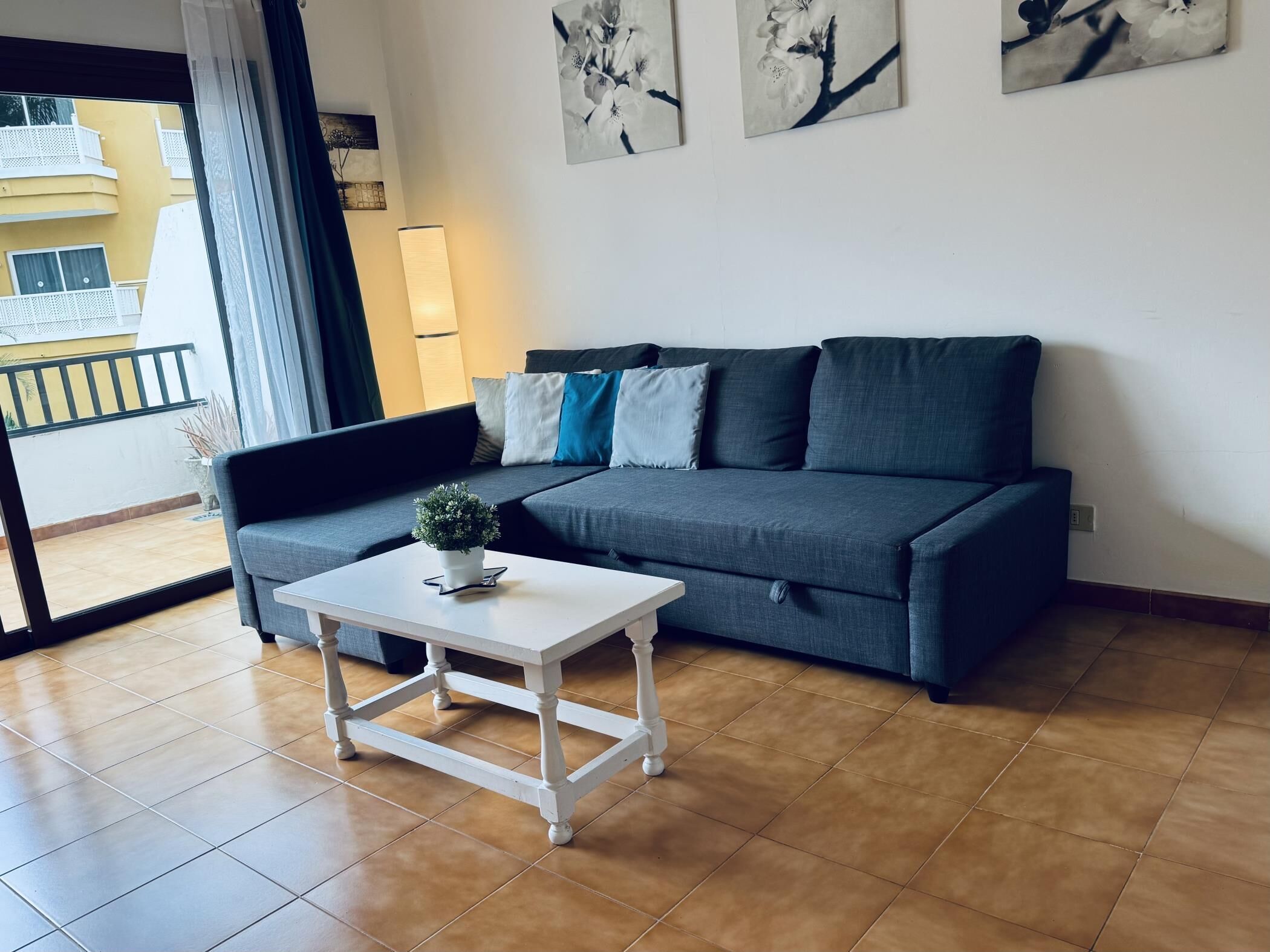 A living room with a grey sofa, a white coffee table with a plant, and artwork on the wall.