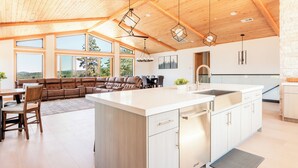 A spacious kitchen with a large island, wooden ceiling beams, and large windows offering views of the outdoors.