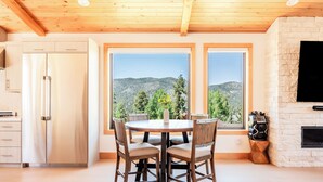 A modern kitchen with a built-in refrigerator, a dining table with chairs, and large windows offering a mountain view.