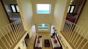 A high-ceilinged room with a central window overlooking a balcony. The room features a white railing, a sofa with cushions, a small table, and a chair. - Bella Vista, Las Terrenas (Las Terrenas)