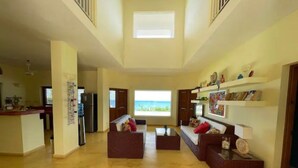 A spacious living area with a high ceiling, a kitchen in the background, and a view of the sea through a large window. - Bella Vista, Las Terrenas (Las Terrenas)