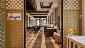 Un hall de hotel con mostrador de recepción, zona de estar y un letrero que dice "WELCOME CAFÉ Reva".