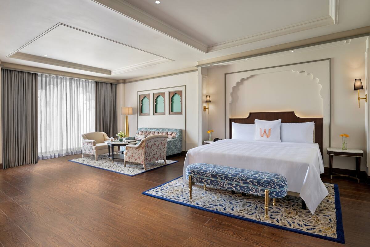 Een hotelkamer met een groot bed, een bureau met stoel, een bank en een groot raam met gordijnen.