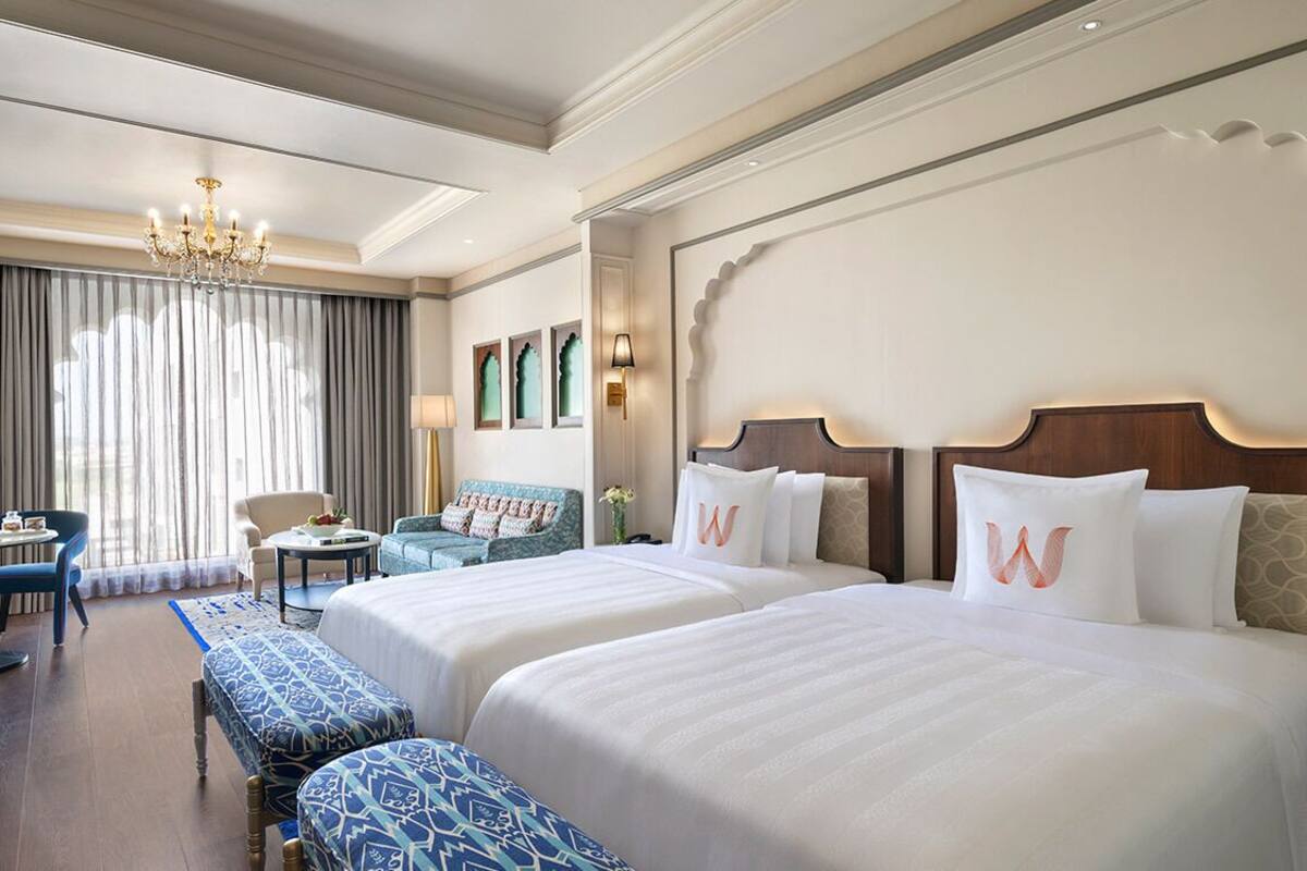 Een hotelkamer met twee bedden, een kroonluchter, een bureau en uitzicht op het omliggende landschap.