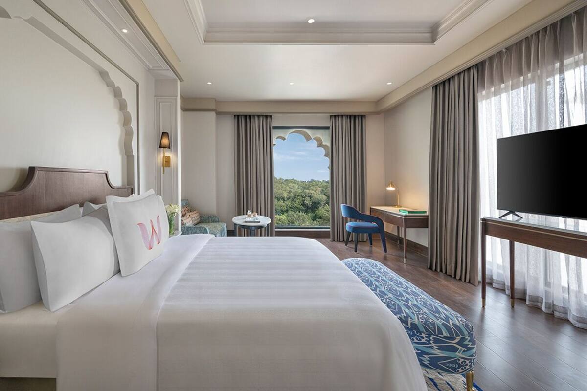 Een hotelkamer met een groot bed, een bureau, een televisie en uitzicht op groen buiten het raam.
