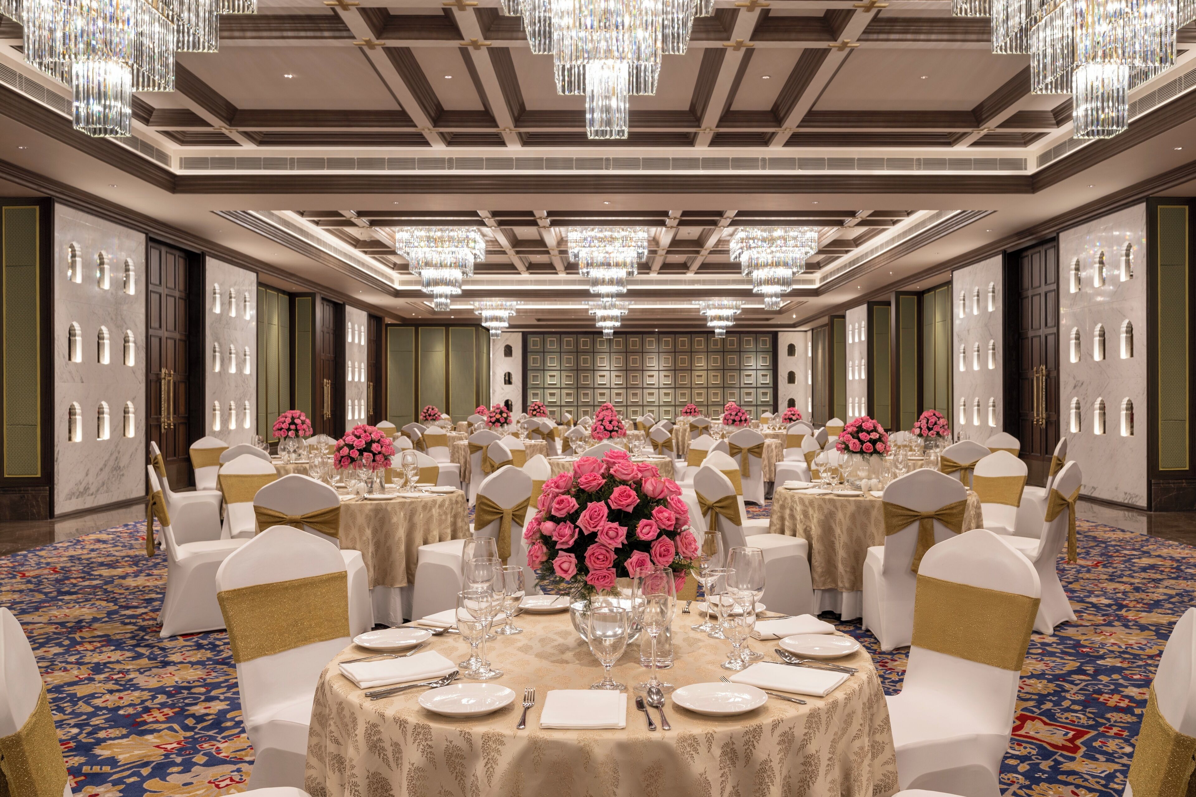 Un salón de banquetes con mesas redondas, sillas blancas y candelabros.